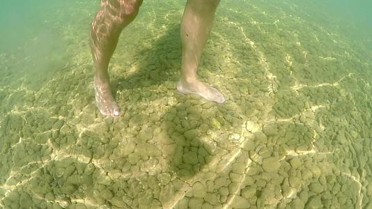 男人的脚在海底用石头和阳光结构行走视频的预览图