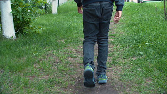 少年男孩在夏季城市绿色草坪上的草地上行走运动鞋视频的预览图