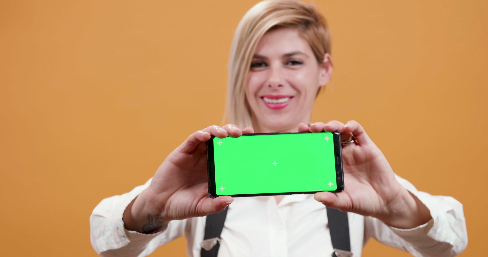 金发色背景下金发女子手里拿着一部带有绿色屏幕的智能手机视频的预览图