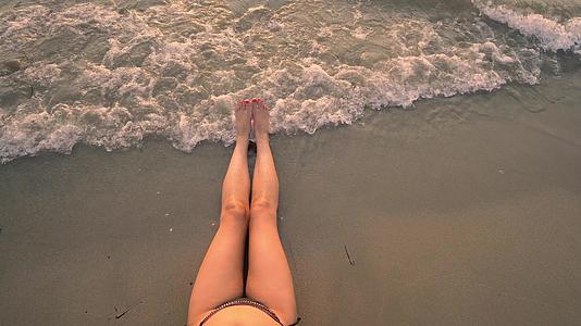 坐在沙滩上穿着性感时尚的双腿看海边的日落视频的预览图