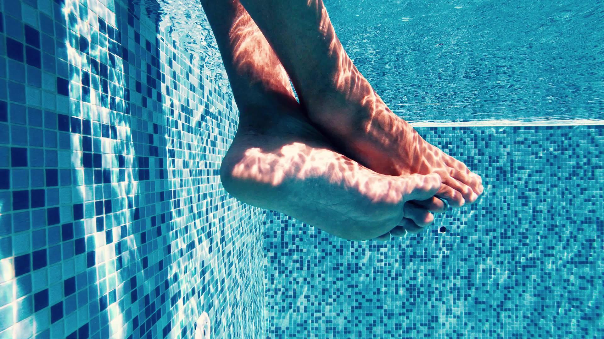 一个人坐在游泳池的边缘在游泳池里鼓励他的腿视频的预览图