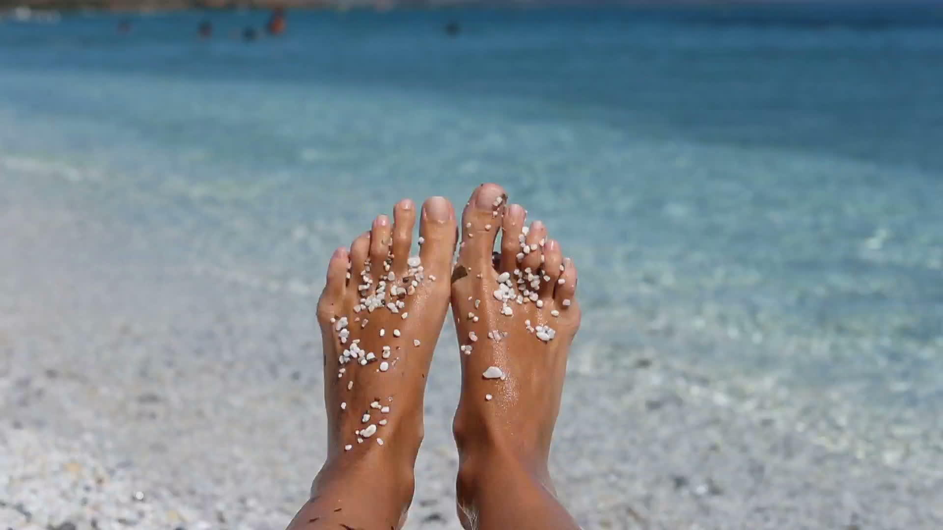 白色沙滩上有石头的女性腿在沙尔地尼亚度假视频的预览图