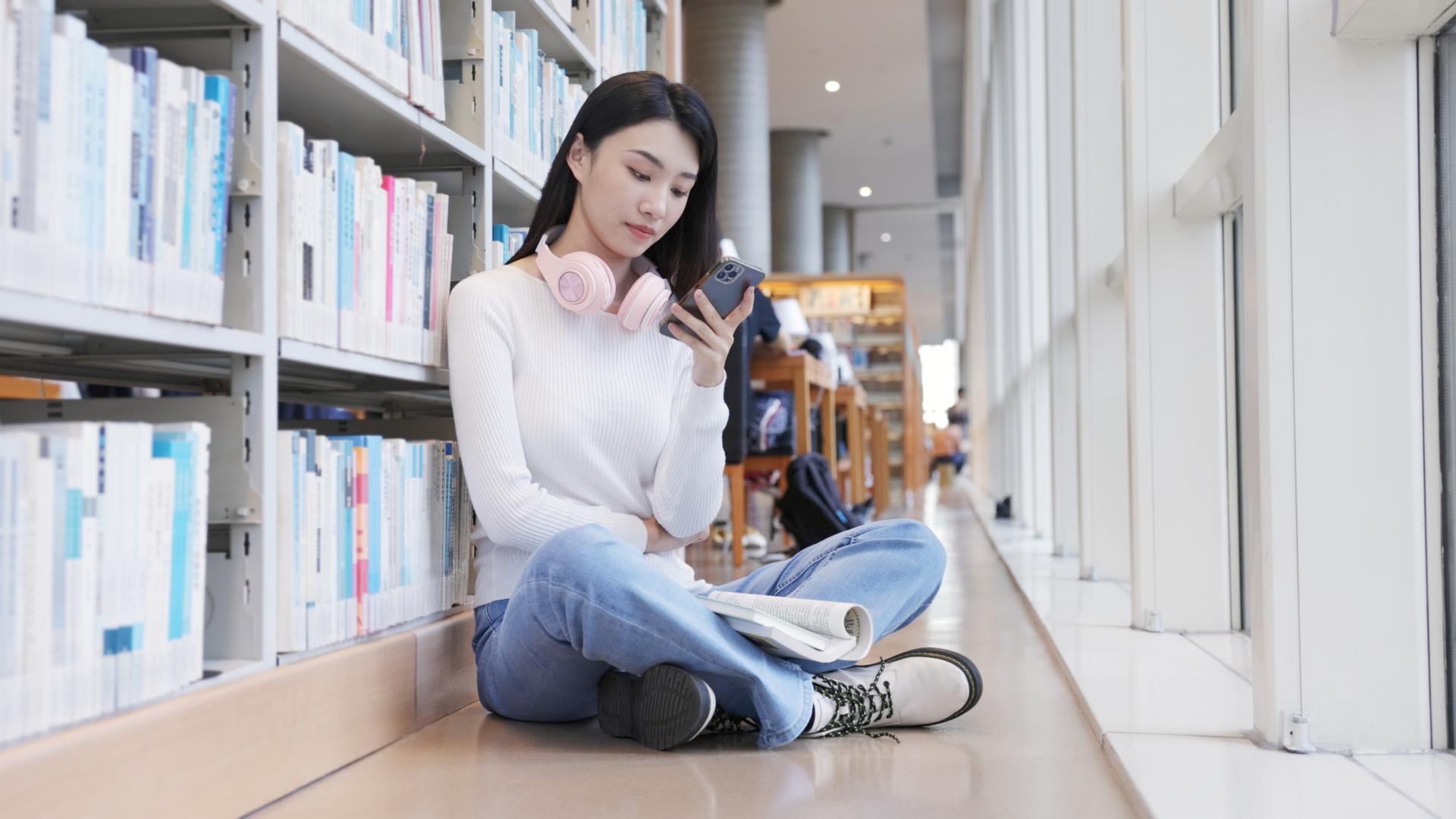 坐在图书馆角落的女大学生正在玩手机视频的预览图