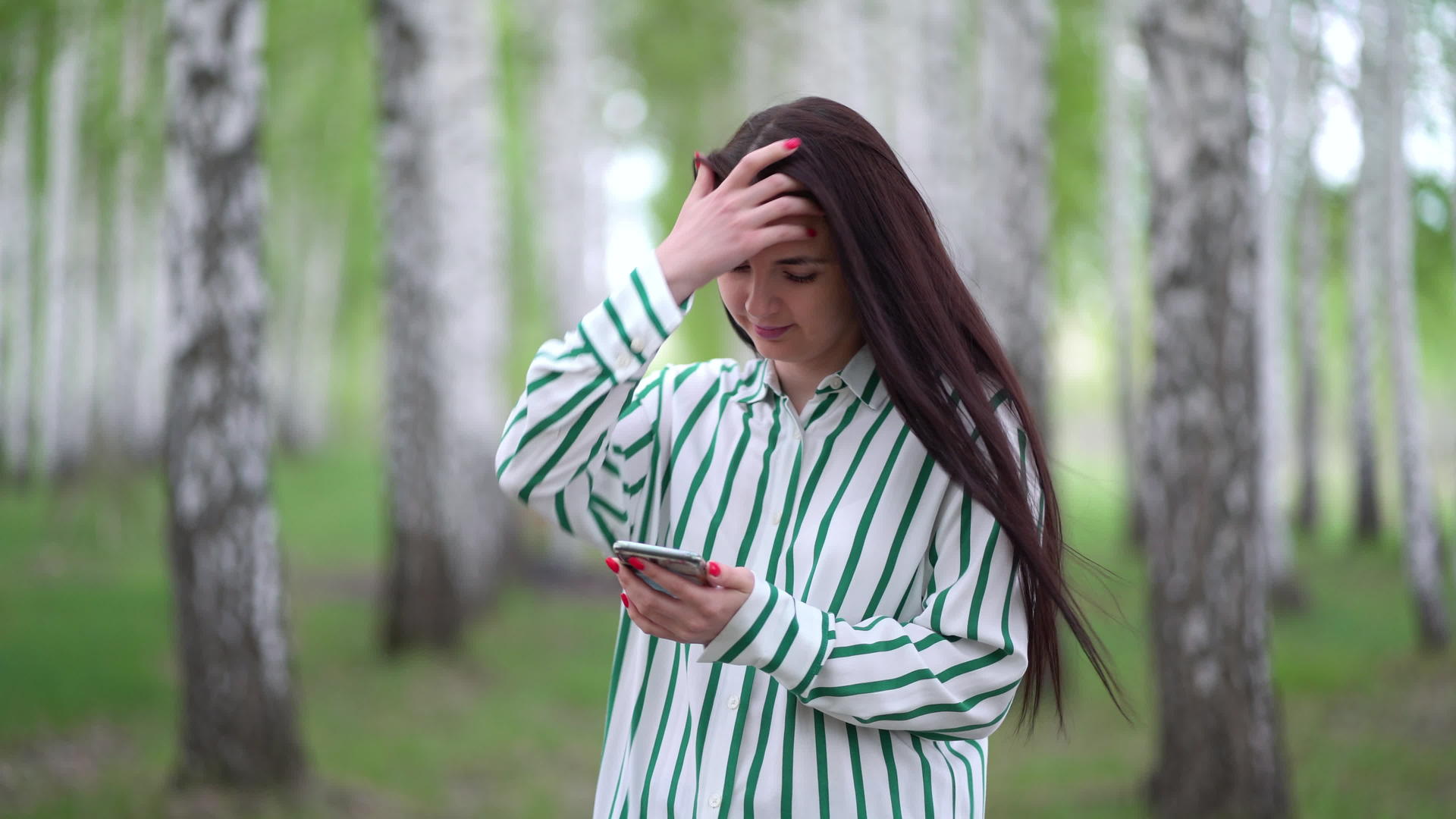 春天美丽的女孩手里拿着智能手机沿着一棵小树走过视频的预览图