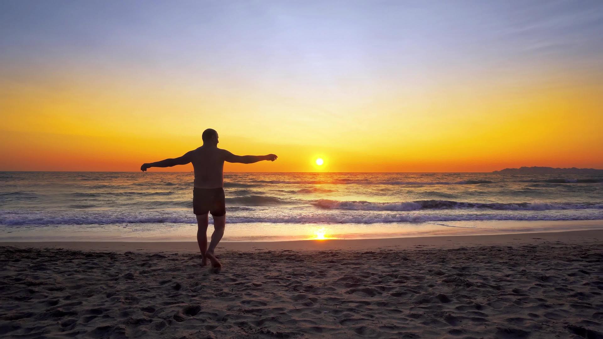 在胜利中男人举起双手站在开阔的海滩上走进水中视频的预览图