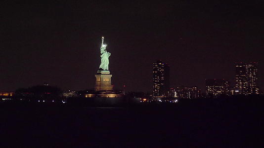 夜间自由雕像照亮纽约城大楼从水中环绕轨道视频的预览图