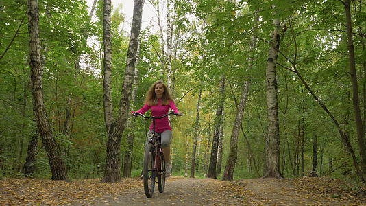 女青年在公园里骑自行车秋天树叶落下向摄像机走去Standicam视频的预览图