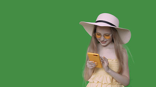 快乐青春期前女孩在夏装和帽子阿尔法频道浏览智能手机视频的预览图