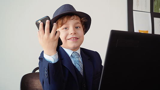 手里拿着手机的男孩商人坐在办公室里微笑着在笔记本电脑附近工作视频的预览图