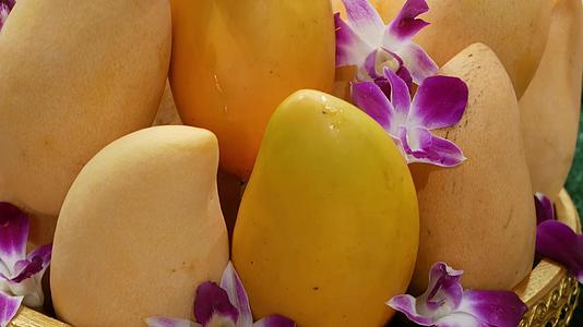 芒果和花的金盘美味成熟的黄色芒果和美丽的紫色兰花视频的预览图