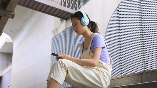 年轻女孩坐在台阶上用手机播放音乐视频的预览图
