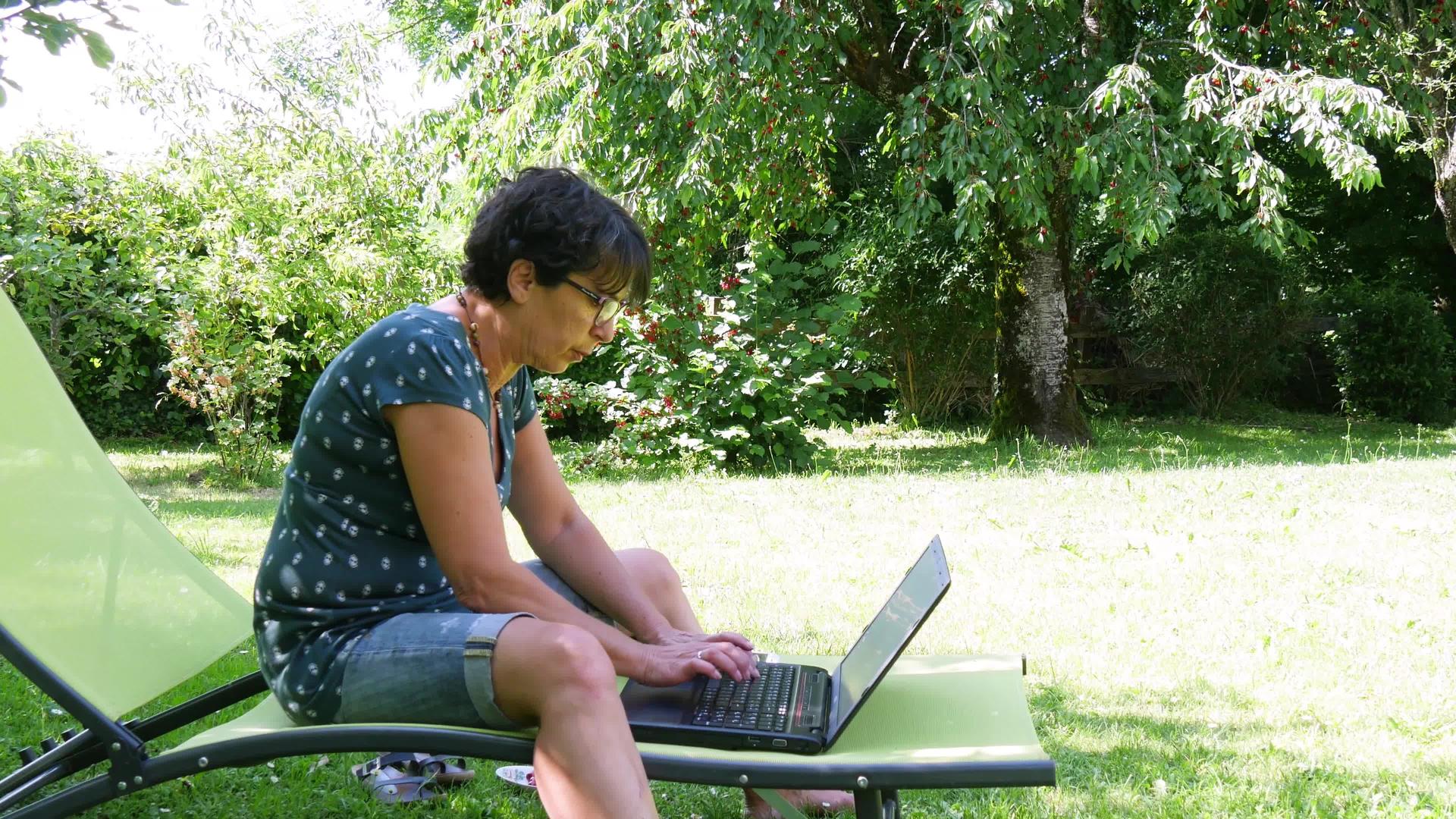 成年妇女在家用笔记本电脑的花园里工作视频的预览图