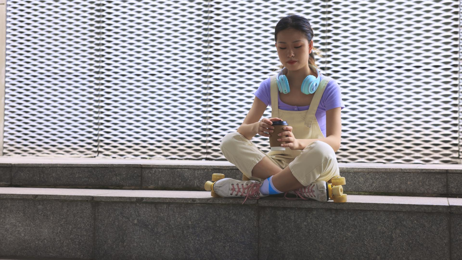 年轻女孩穿着轮滑鞋坐在台阶上喝咖啡休息视频的预览图