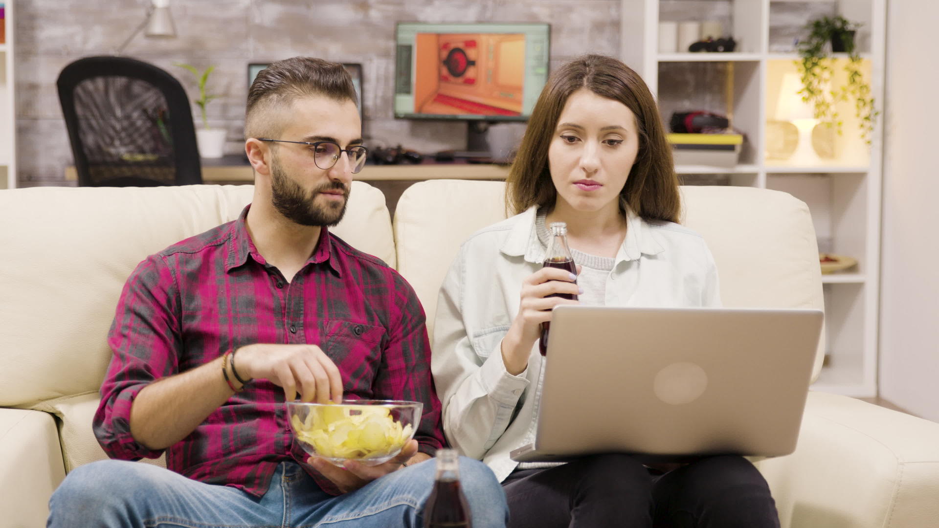 一对夫妇一边喝苏打水一边吃薯片一边浏览笔记本电脑视频的预览图