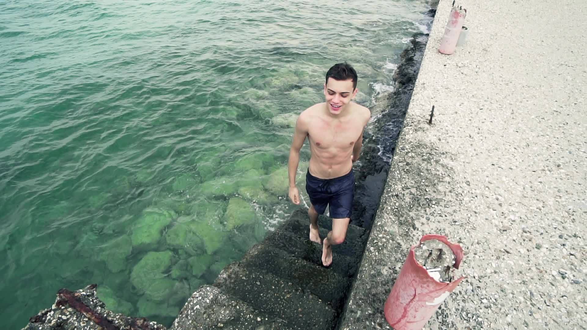 英俊的男孩穿着短裤的肖像在游泳后从水里流出来视频的预览图