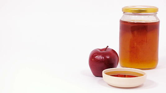 红苹果、一罐蜂蜜和一碗蜂蜜在白色背景下被孤立视频的预览图