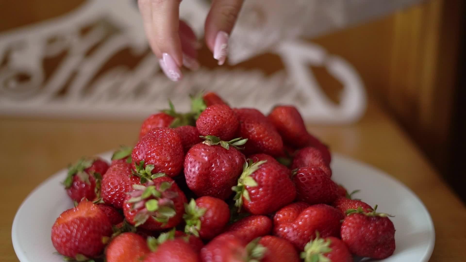 年轻女孩从盘子里吃红色甜草莓视频的预览图