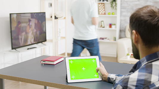 男人在数字平板电脑上滚动在明亮的客厅里用绿色屏幕滚动视频的预览图