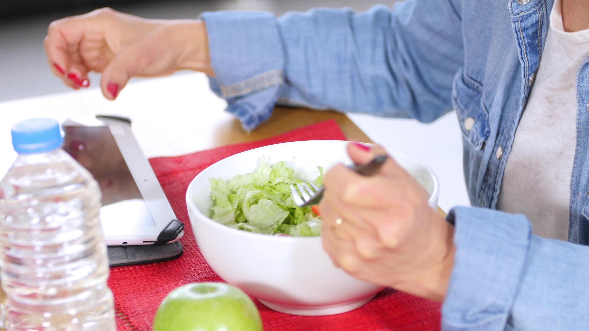 吃沙拉时女性用数字平板紧握手视频的预览图