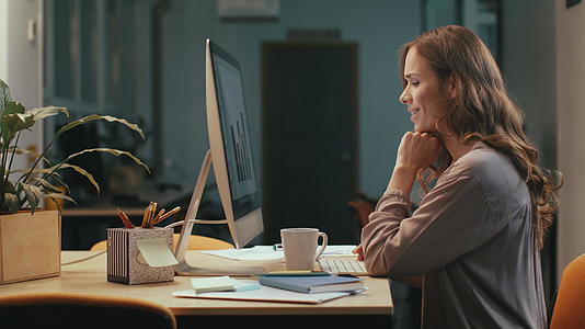 商业女性在夜间工作时阅读电脑财务报告视频的预览图