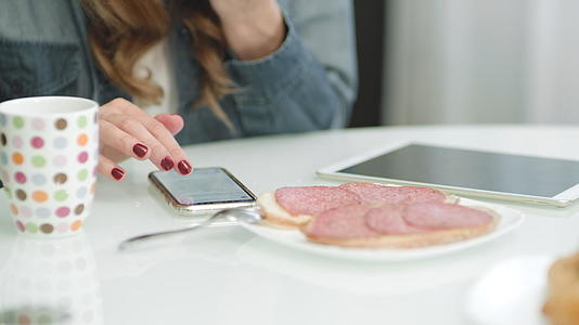 女性在吃三明治时用手机滚动视频的预览图