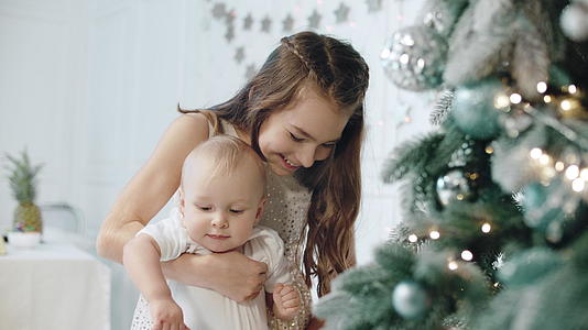 快乐女孩在现代住宅的圣诞树旁抱着孩子视频的预览图