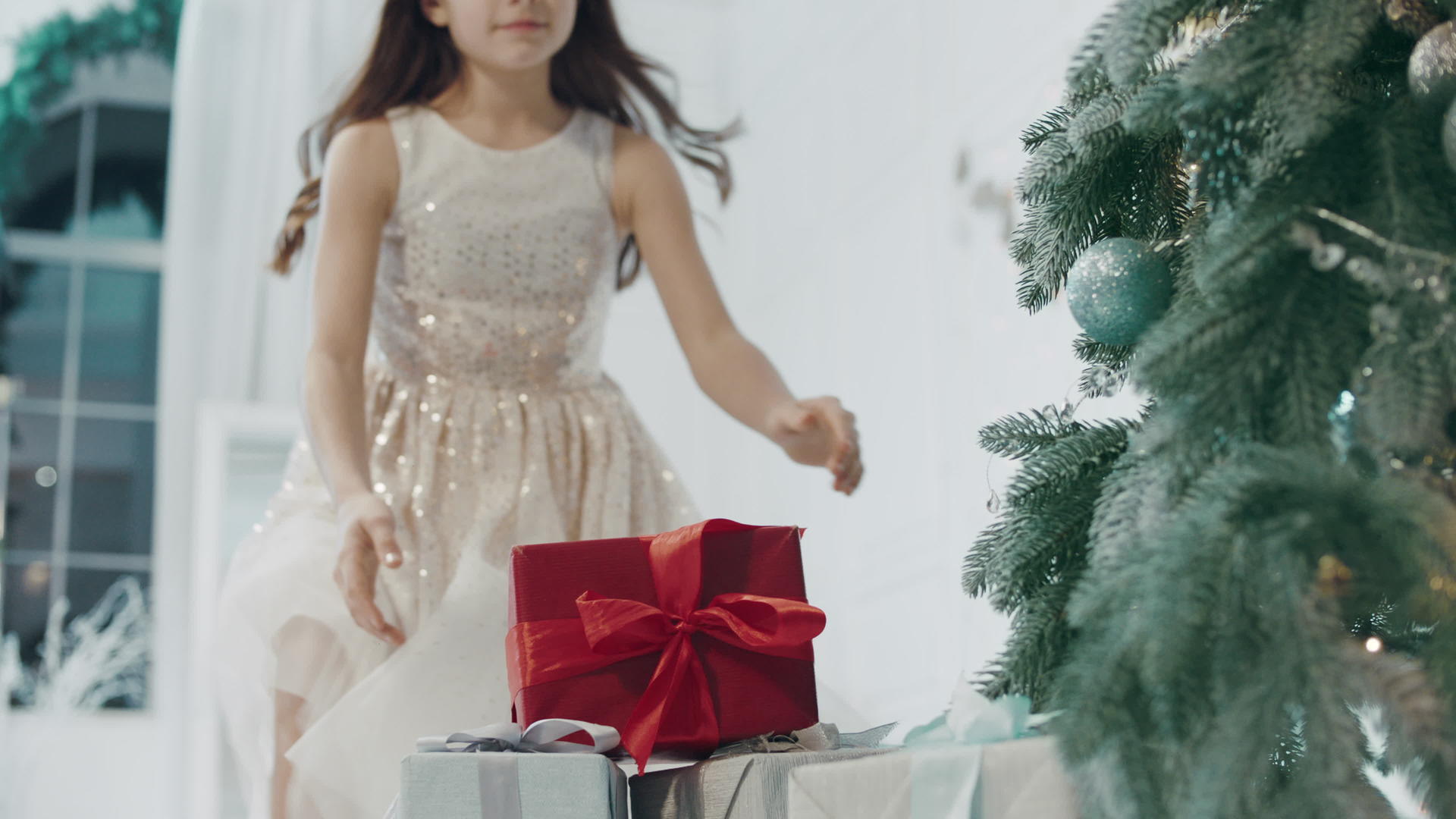 快乐的女孩在现代公寓的圣诞树附近拿着礼物盒视频的预览图