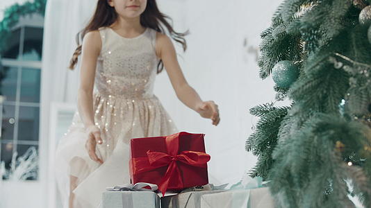 快乐的女孩在现代公寓的圣诞树附近 拿着礼物盒视频的预览图