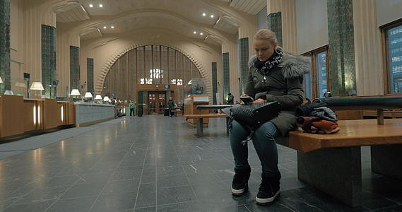 在车站大厅等候的妇女和使用智能手机视频的预览图