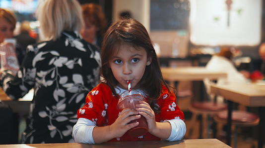 小黑发女孩坐在桌子上喝着沙冰视频的预览图