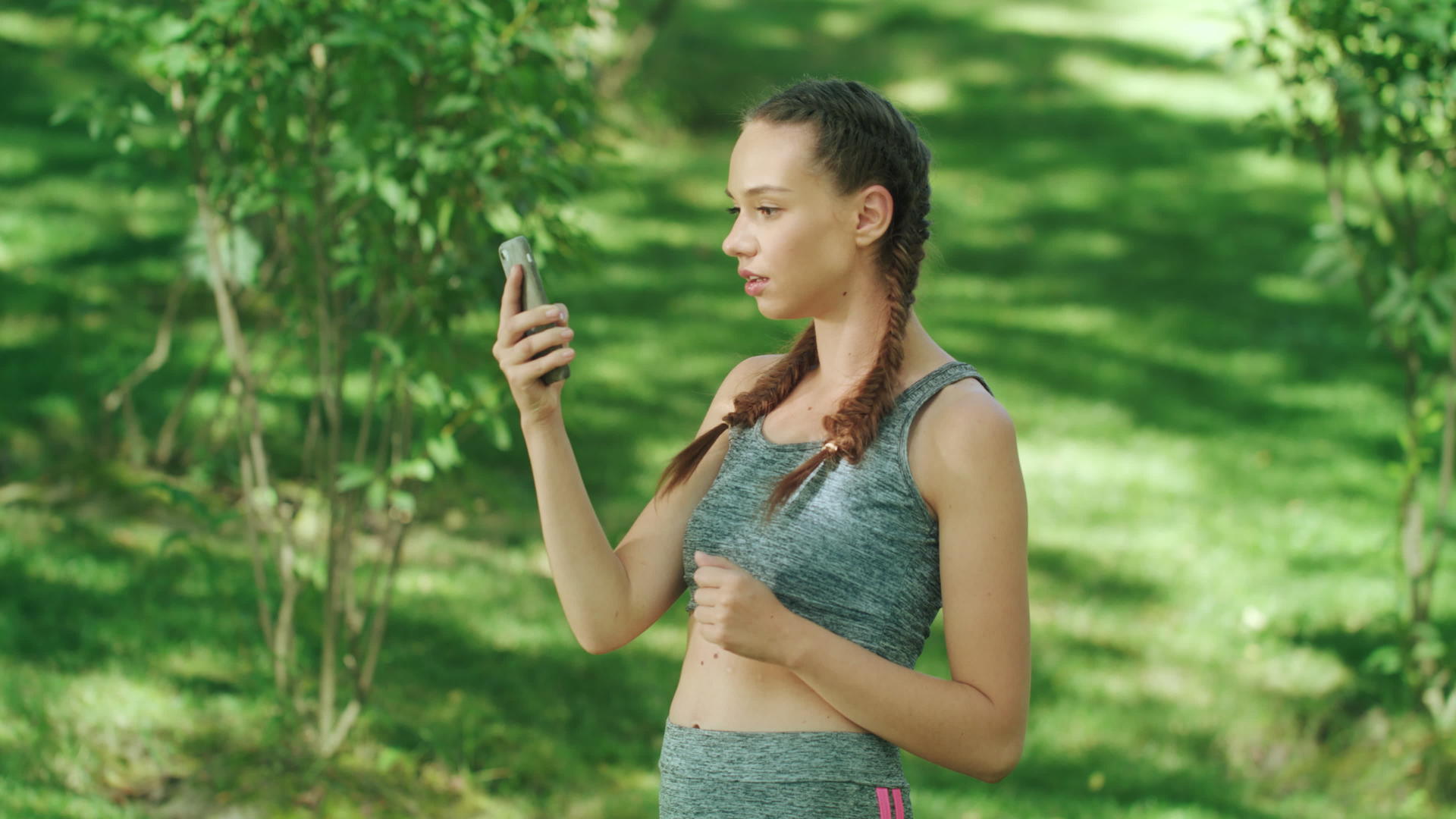 快乐的女跑步者在夏季公园慢跑时在手机应用程序中查看结果视频的预览图