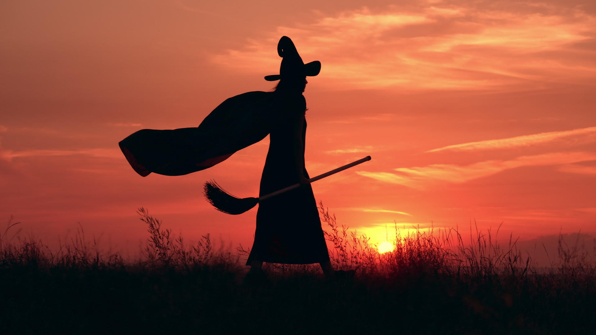 穿着漂亮裙子的女巫拿着扫帚在田野里散步视频的预览图