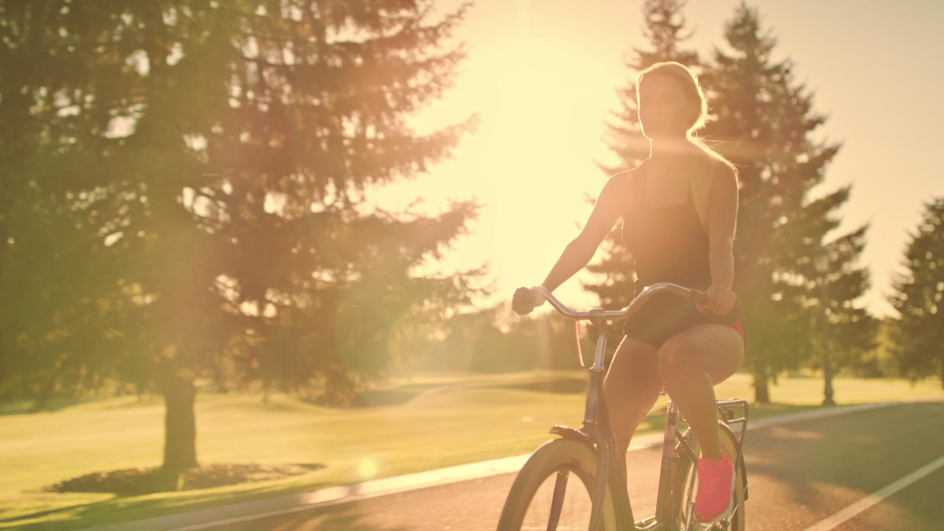 健身女性在金色日落风景的夏季公园骑自行车视频的预览图