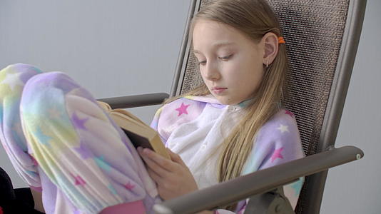 一个穿着睡衣在椅子上看书的专注女孩视频的预览图