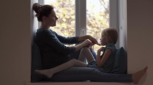 年轻的孕妇用绿色的衣服在窗台上抽女儿的风视频的预览图