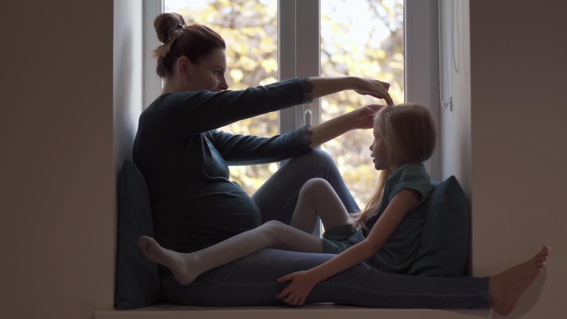 年轻怀孕的女孩在窗台上的绿色绿色的石头上做发型视频的预览图