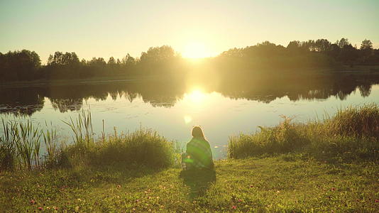 孤单的女孩坐在湖边裹着格子看着日出视频的预览图