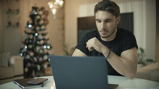 男人在圣诞树上用笔记本电脑视频的预览图
