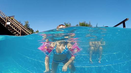 快乐的女孩在漂浮在水面上的游泳池里带着臂带在水面上漂浮飞到相机视频的预览图