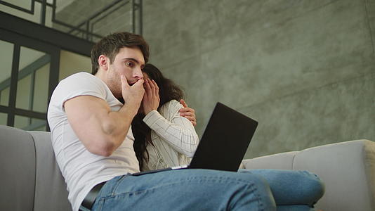 一对受惊的夫妇看着沙发上电脑屏幕上的肖像视频的预览图