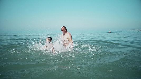 男人和儿子在日落时在热带海滩上互相泼水视频的预览图