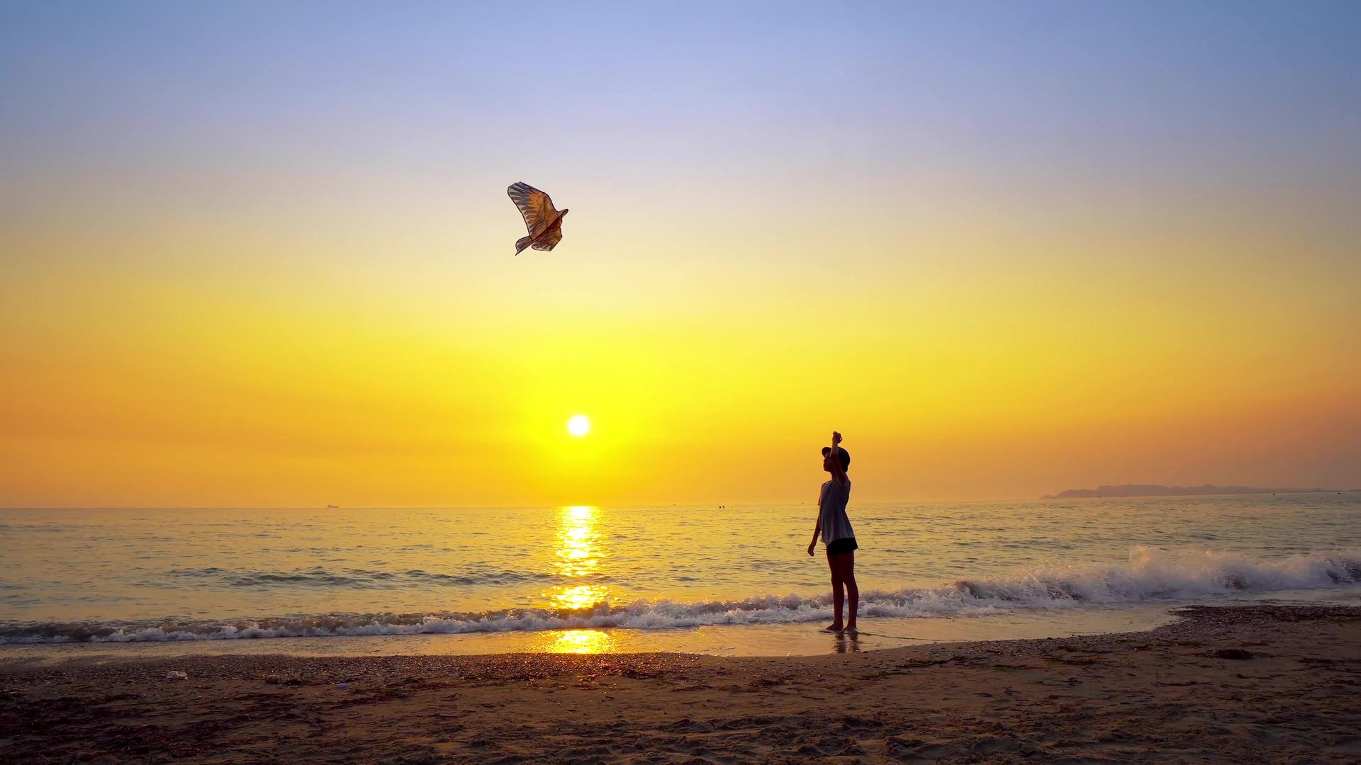 暑假期间男孩在日落的空海滩上玩帽子风筝视频的预览图