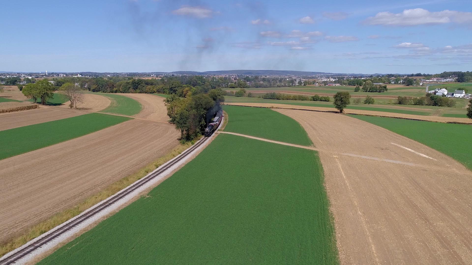 古老的蒸汽客运列车沿着农场和农村的空中航向视频的预览图