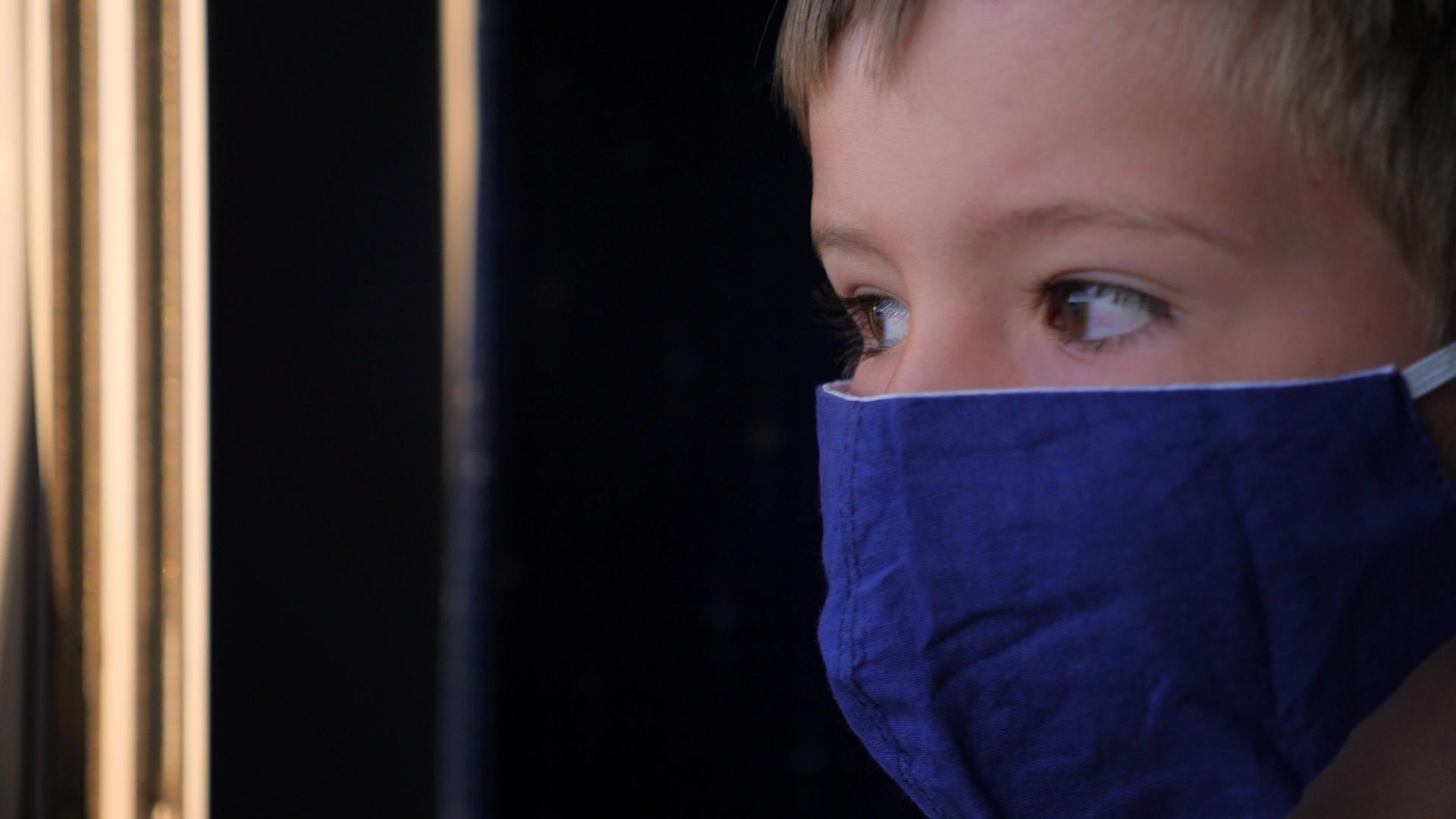 一个戴着口罩的男孩看着外面的火车窗视频的预览图