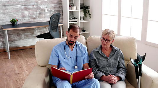 养老院的男护士为老年妇女读一本书视频的预览图