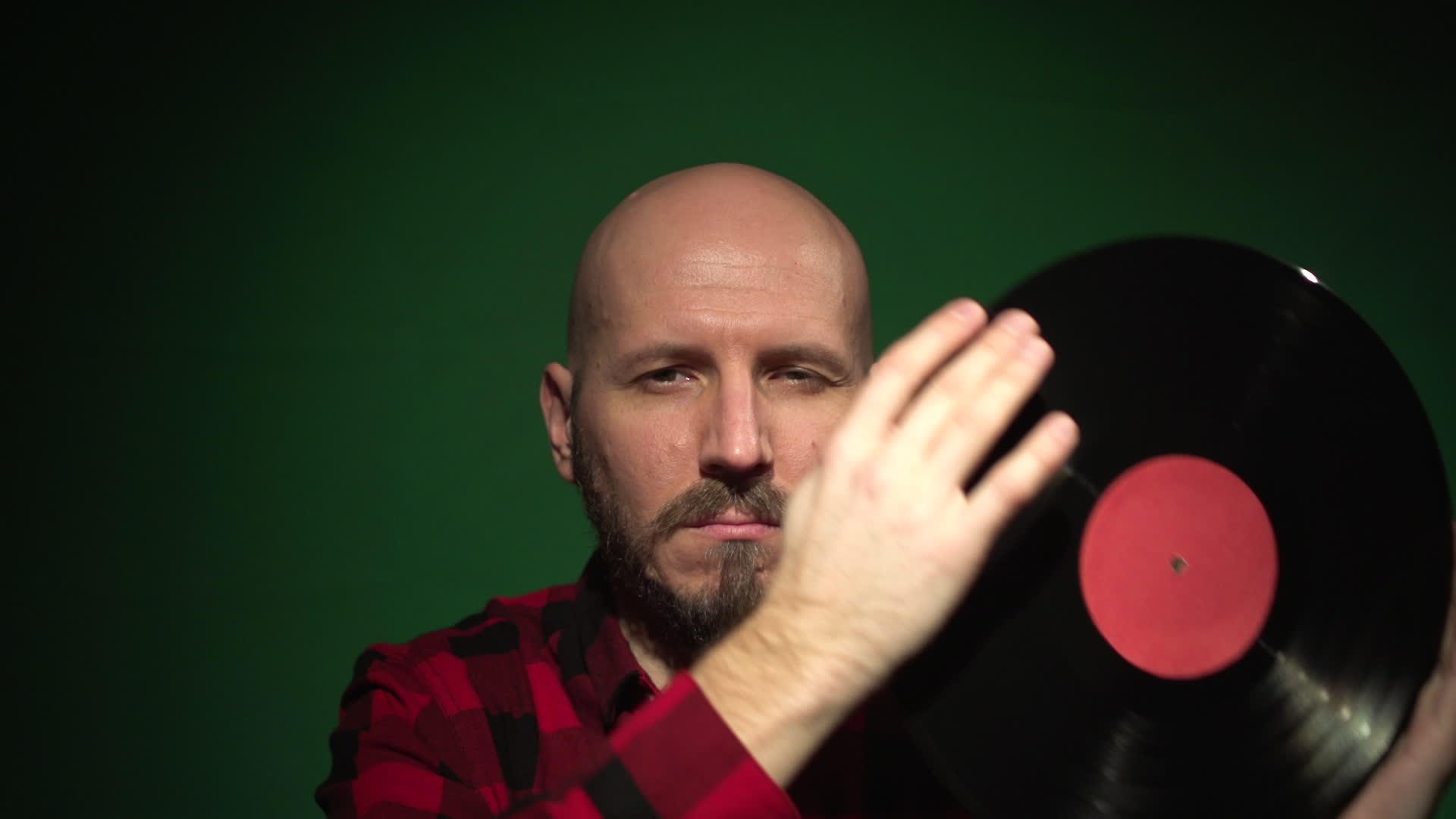 红色格子衬衫的秃头男子躲在红色黑胶唱片后面视频的预览图