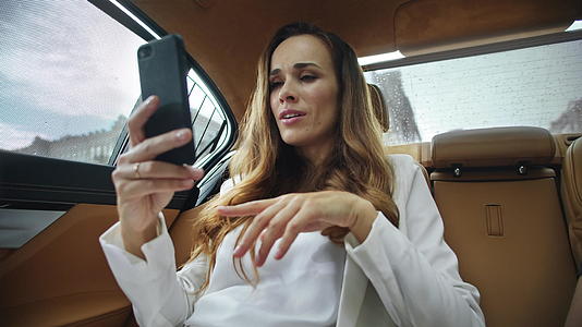 业余女商人在现代汽车中使用智能手机进行视频电话交谈视频的预览图