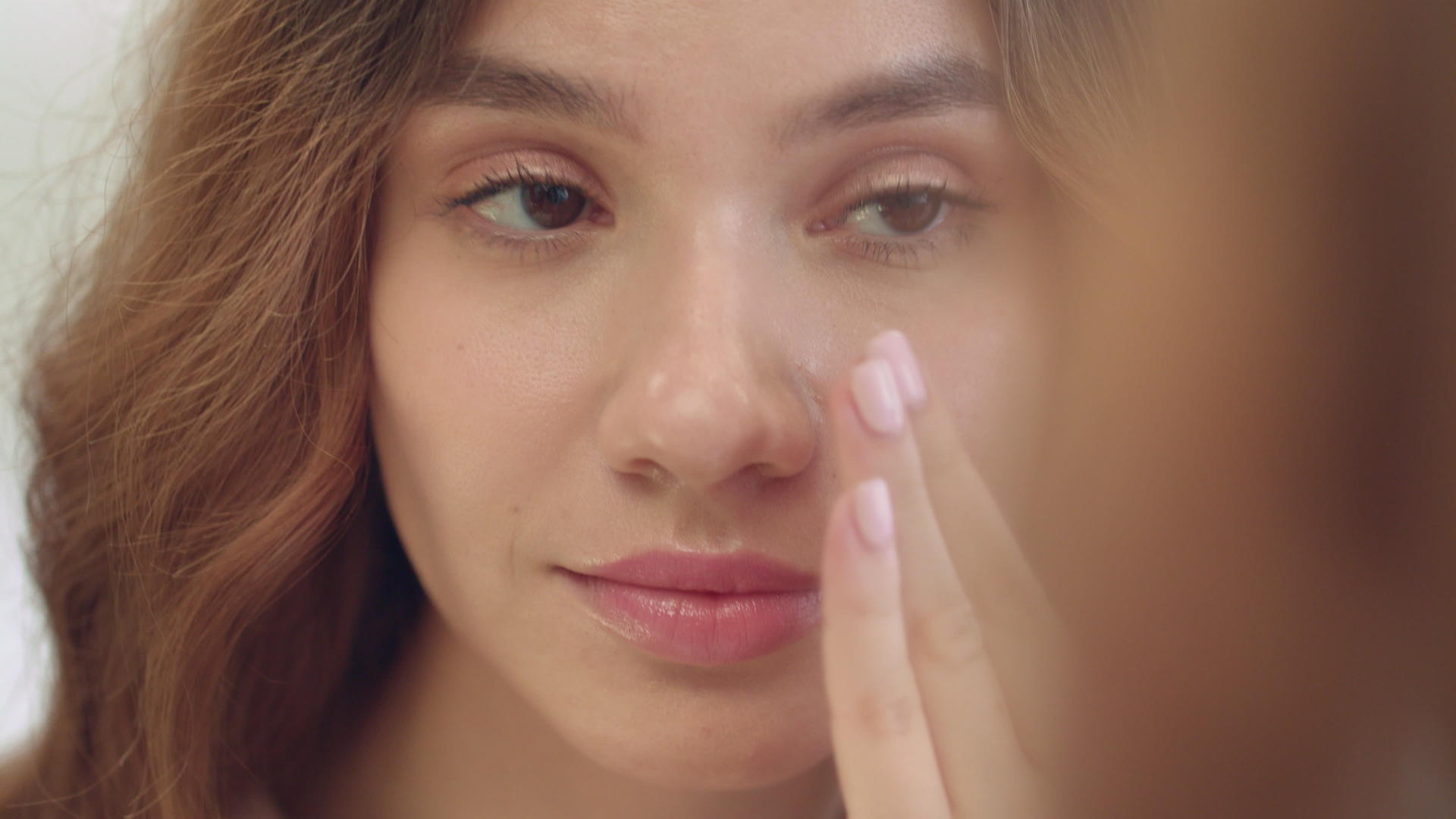 微笑的女人在面部皮肤前面的浴室镜子上涂抹湿霜视频的预览图
