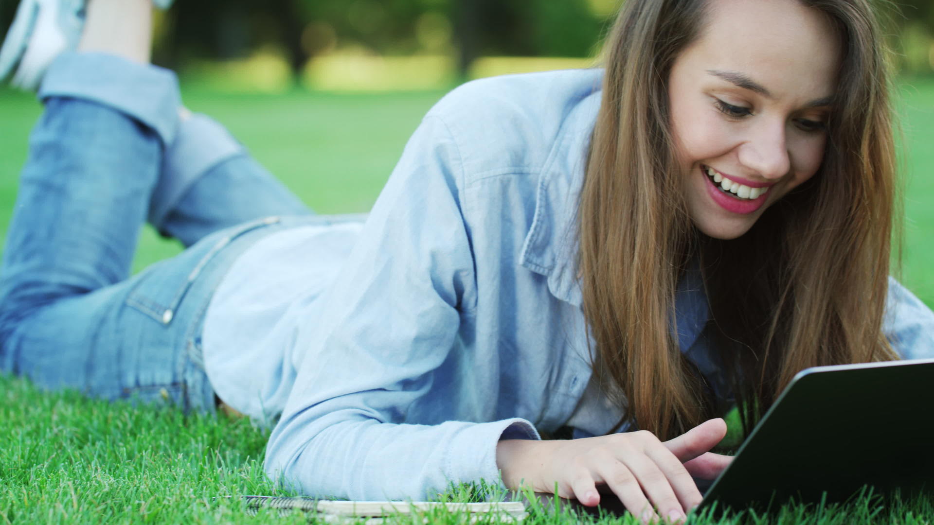 女性躺在绿色的草地上使用笔记本视频的预览图