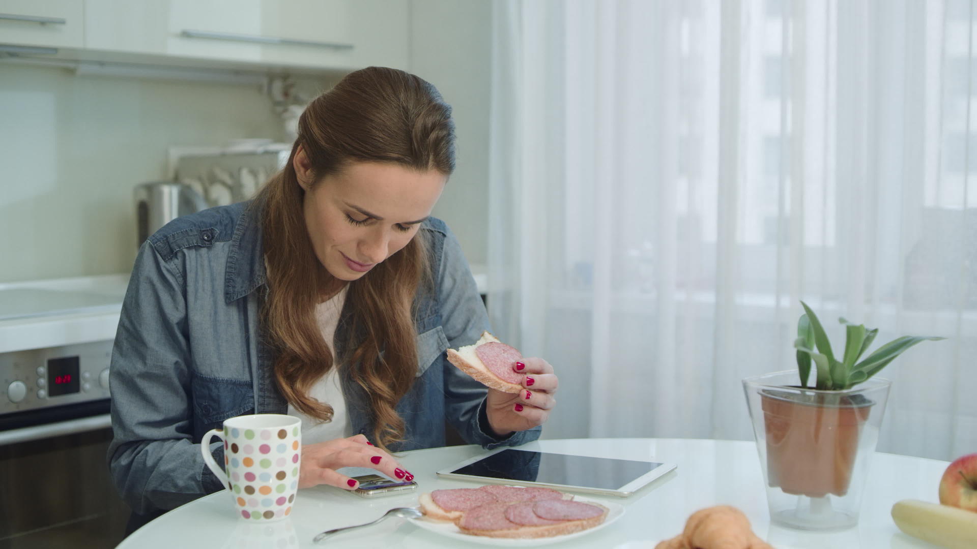 在现代厨房早餐时微笑的女性会说智能手机视频的预览图